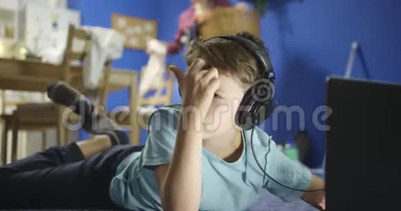 小男孩躺在硬木地板上通过耳机听音乐的肖像视频的预览图