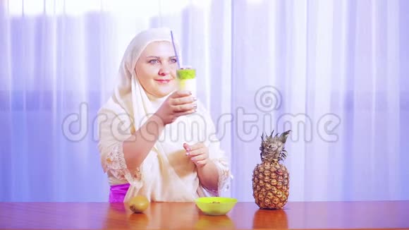 一位身穿浅色围巾的年轻穆斯林妇女展示了一杯鸡尾酒和水果并微笑着视频的预览图