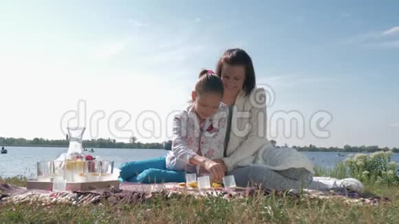 爱妈妈小女孩在放松的时候给妈妈喂饭在天气不好的时候在拉夫附近的草坪上家庭野餐视频的预览图