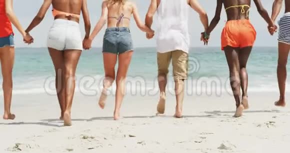 一群混血朋友手牵手在海滩上奔跑视频的预览图