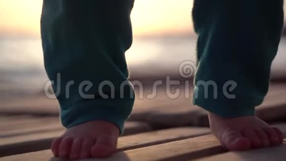 日落时分一个美丽的小男孩在海边的一个木制休息室上爬行视频的预览图