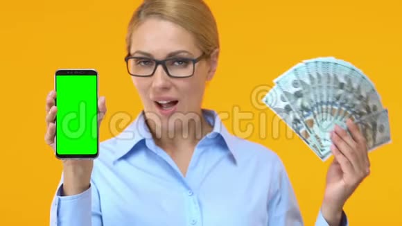 漂亮的商务女性带绿色屏幕的智能手机和一堆美元视频的预览图