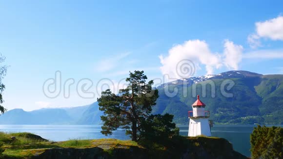 在一个阳光明媚的日子里白色灯塔塔上有红色的顶部和附近的杉树沿着挪威峡湾两岸的山视频的预览图