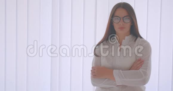 戴眼镜的白种人年轻女子的特写镜头双臂交叉在胸前站在室内视频的预览图