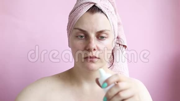 一个穿着毛巾的年轻女孩在淋浴后擦过面霜脸部按摩上午自理视频的预览图