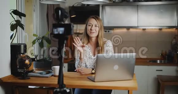 快乐流行的年轻金发女性vlogger拍摄新的博客视频与专业相机在家厨房慢动作视频的预览图