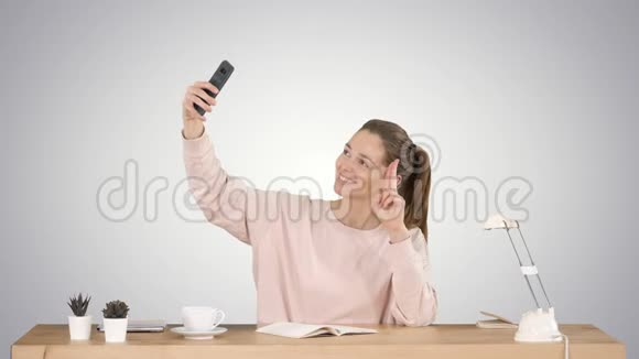 美丽的女人自拍她的手机坐在桌子上的梯度背景视频的预览图