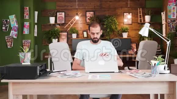 年轻的创意总监坐在办公室打开他的笔记本电脑视频的预览图