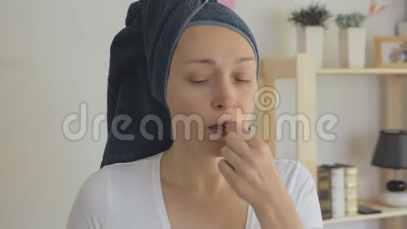 一位戴着毛巾的女性家庭主妇用杯子里的水吞下药丸视频的预览图