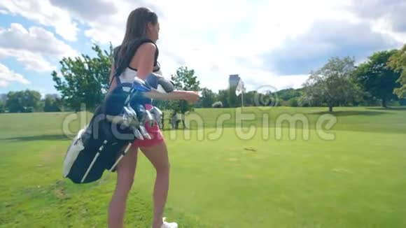 带着高尔夫球配件的年轻女士正沿着草坪散步视频的预览图