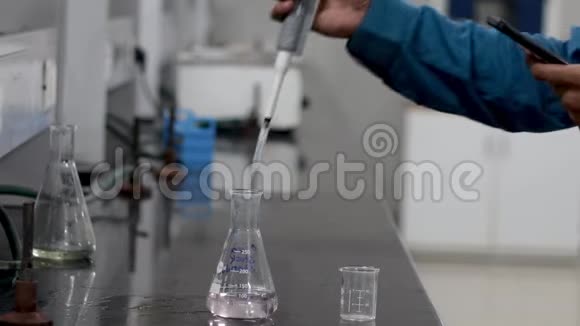 一位研究科学家用一个微型吸管将无色化学物质从锥形烧瓶中倒入烧杯的手视频的预览图