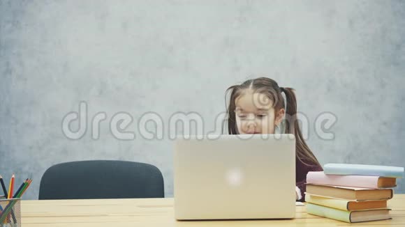 快乐可爱的聪明女孩坐在桌子上的一叠书和笔记本电脑的肖像复制空间教育与发展视频的预览图