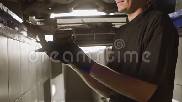 机械师站在车坑里在修理汽车站悬架修理车辆坑前戴着手套视频的预览图