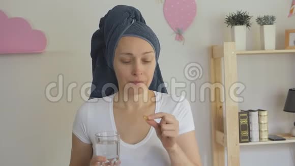 一位戴着毛巾的女性家庭主妇用杯子里的水吞下药丸视频的预览图