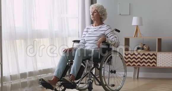 一个体贴悲伤的老妇人独自坐在轮椅上视频的预览图