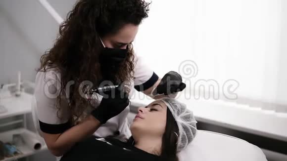 穿着卷发白色长袍的美容师正在为女性画眉或用针修正眉毛视频的预览图