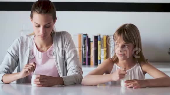 年轻漂亮的妈妈和女儿在家吃酸奶时互相看着视频的预览图