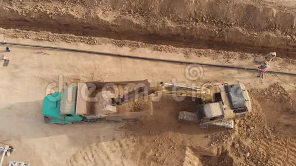 挖掘机将土壤装载到运输卡车上顶部向下的空中镜头视频的预览图