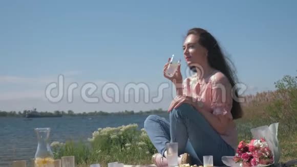 大自然中的野餐快乐的女性在河边放松时喝柠檬水和吃零食视频的预览图