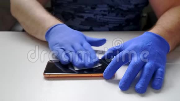 男性手中的蓝色手套取代了一个破碎的钢化玻璃屏幕保护器的智能手机一个男人准备智能手机视频的预览图
