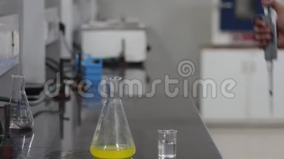 一位科学家的手把一种无色的化学物质从一个微型吸管倒入一个锥形的黄色化学物质视频的预览图