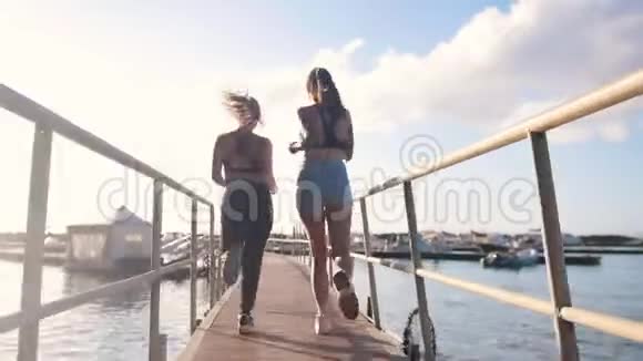 两个穿着运动服的年轻女子在桥上朝海港跑去视频的预览图