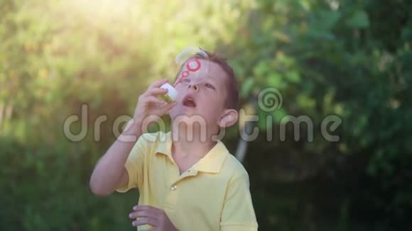 小男孩在大自然的绿色背景下吹肥皂泡视频的预览图