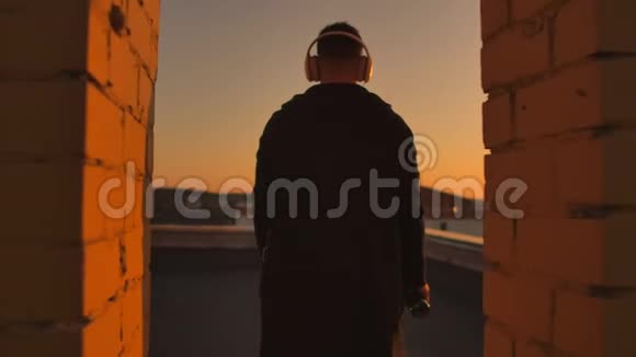 日落时分一个人戴着耳机走在屋顶上从日落时分摩天大楼的高度看着这座城市放松放松视频的预览图