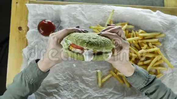 美甲的女人手里拿着一个多汁的大汉堡里面有一个肉包和一个绿色的面包视频的预览图