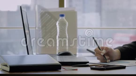 手握女性创意总监坐在办公桌上用铅笔记录图表视频的预览图
