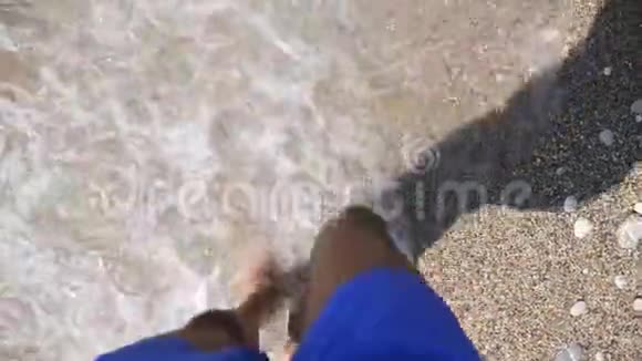 在阳光明媚的日子里人们赤脚在海岸上慢慢行走小浪溅落在年轻人的脚上漫步在沙滩上视频的预览图