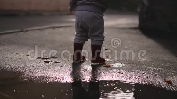 小幼儿穿着红色雨靴在水坑里玩愉快的秋季活动视频的预览图