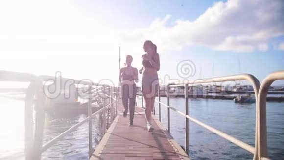 两个穿着运动服的年轻女子在海港背景下的桥上慢跑视频的预览图