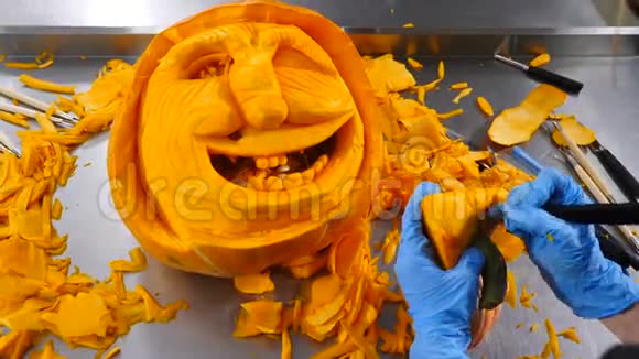 无法辨认的人雕刻南瓜万圣节庆典4K双手戴蓝色手套切橙色菜视频的预览图
