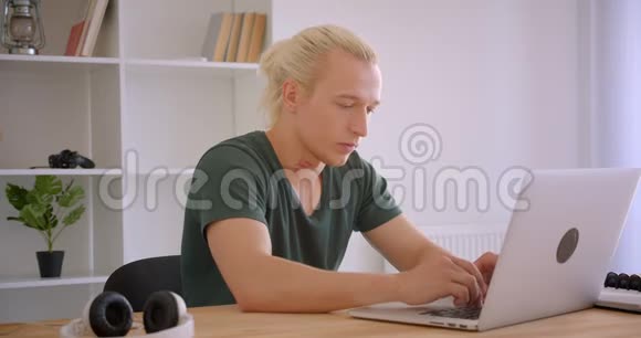 年轻的金发时髦商人在笔记本电脑上打字在办公室里看着相机的特写照片视频的预览图