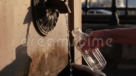 在公园里女人的手把一个透明的瓶子放在阳光下的水流下视频的预览图