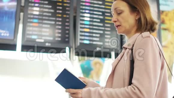 成熟的女人独自站在机场航班时刻表附近查看离境信息委员会视频的预览图