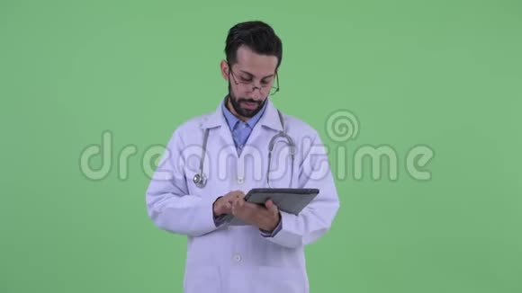 快乐的年轻留胡子的波斯医生在用数码平板电脑说话视频的预览图