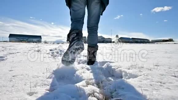 在一个冬天阳光明媚的日子里跟随着穿着牛仔裤和温暖鞋子在雪地里行走的男人特写低角度回去视频的预览图