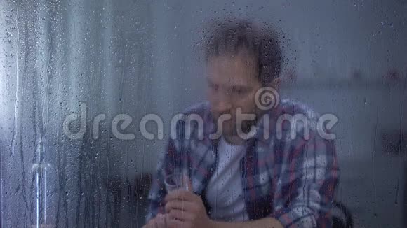 嗜酒成瘾的人在雨窗后孤独地喝伏特加视频的预览图