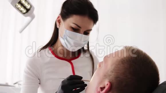 戴口罩的女牙医检查病人的口腔他坐在牙科椅上负责牙科治疗视频的预览图
