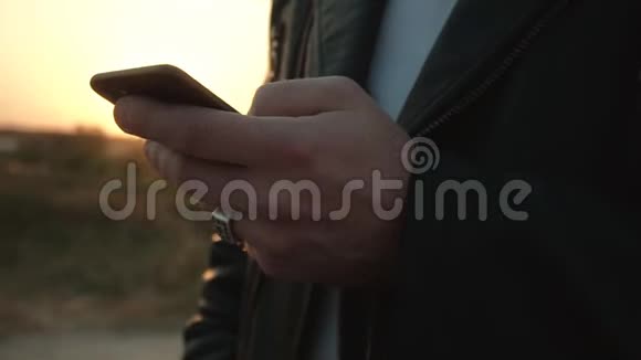 在阳光明媚的日落背景下一个男人把手指放在智能手机屏幕上特写背景慢视频的预览图