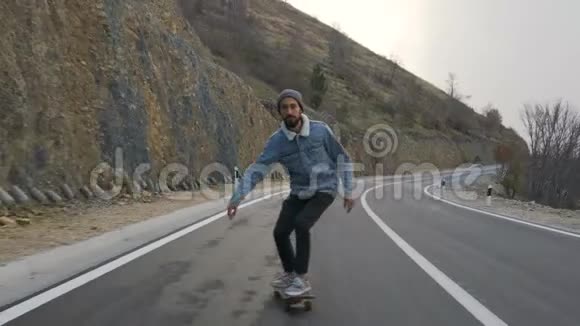 有胡子的年轻人骑着滑板在乡间小路上下山视频的预览图