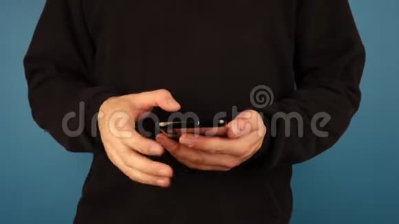 一个穿着黑色套衫的男人在面对蓝底相机时使用手机视频的预览图