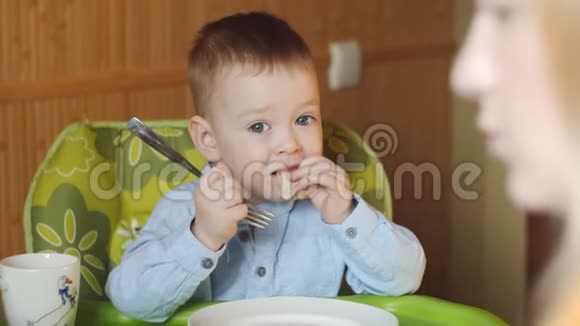 小男孩坐在厨房和盘子里的儿童座位上是非常美味的食物微笑和玩耍视频的预览图