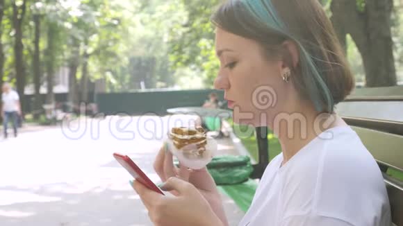 迷人的女人在智能手机和吃蛋糕上阅读信息视频的预览图