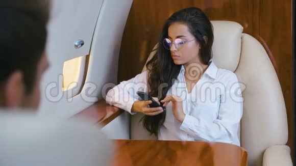 漂亮的商务女性戴眼镜手里拿着智能手机乘坐私人飞机旅行商务旅行视频的预览图
