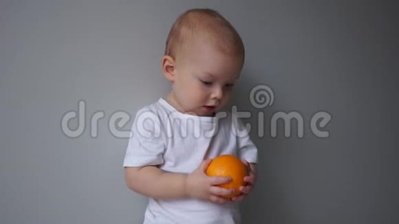 这孩子手里拿着一个橘子一个两岁蓝眼睛男孩的肖像健康饮食视频的预览图