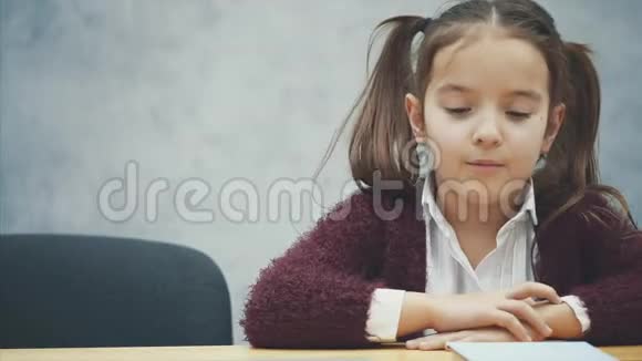 一个女学生坐在桌子旁在此期间选择一本书或笔记本电脑在灰色背景下快乐视频的预览图
