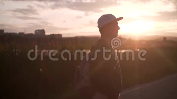 一个戴着帽子和背包的年轻人在夕阳的灯光下在城市的背景下疯狂的风景视频的预览图